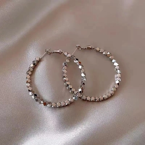 Close-up of silver geometric polyhedron bead hoop earrings on beige silk fabric