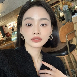 Close-up of a silver twisted hoop earring worn by a model in a cozy cafe setting