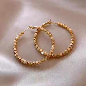 Detailed close-up of golden hoop earrings with faceted geometric beads on satin