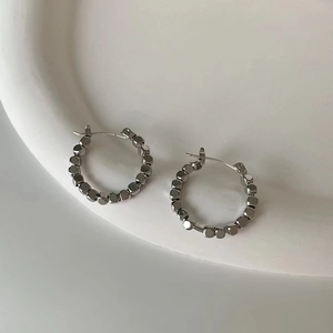 Close-up of geometric textured silver hoop earrings on a white ceramic display tray