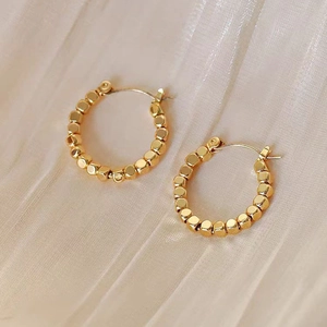 Macro detail of gold beaded hoop earring with geometric texture on velvet fabric