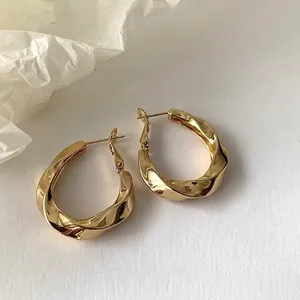 Close-up of golden twisted hoop earrings with irregular geometric design and mirror finish
