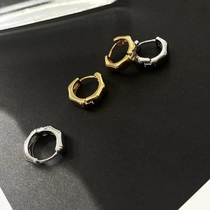 Detail shot of small gold and silver bamboo-style hoop earrings on a dark matte surface