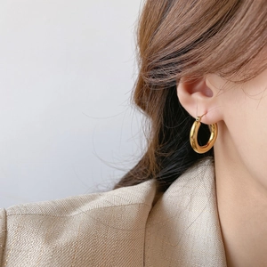 Orecchini a cerchio intrecciati placcati oro 18K indossati da una modella con giacca beige