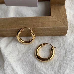 Dettaglio di orecchini a cerchio ritorti placcati in oro 18K su un panno di lino pulito