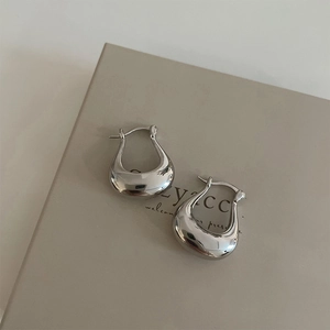 Detailed close-up of polished silver U-shaped earrings on a neutral display board