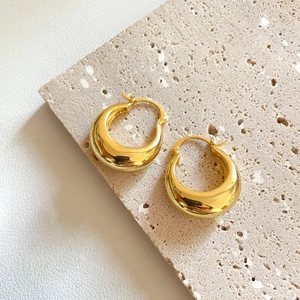Détails de boucles d'oreilles créoles dorées épaisses sur pierre et cuir texturé