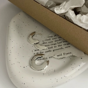 Detailed view of silver hoop earrings on a ceramic tray with vintage paper accents