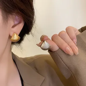 Detail of gold and silver shell-shaped stud earrings with 3D ribbed vertical textures