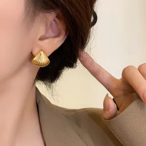 Close-up of gold shell earrings with ribbed texture on model showing the size and fit