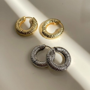 Close-up of gold and silver textured metal hoop earrings with lava-like matte finish