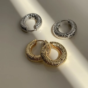 Detail of gold and silver hoop earrings with hammered metal texture on beige background