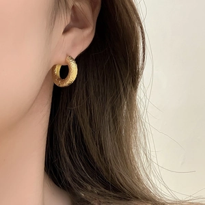Golden textured hoop earrings with a hammered finish shown on a model's ear