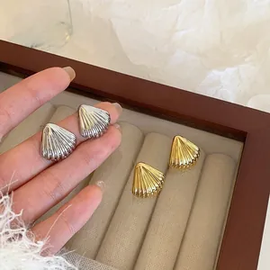 Detailed view of shell-shaped stud earrings in gold and silver with ribbed texture