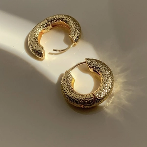 Detail of chunky gold hoop earrings with hammered texture and artistic caustic shadows