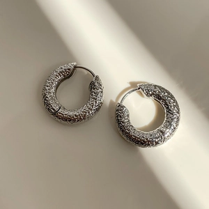 Detailed close-up of silver hoop earrings with unique hammered metal lava texture
