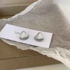 Macro detail of silver seashell stud earrings with textured ridges on a white display card
