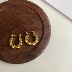 Vue détaillée de créoles torsadées plaquées or 18 carats sur plateau en bois