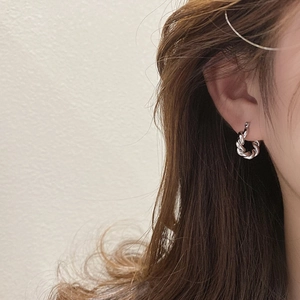 Gros plan de boucles d'oreilles créoles argentées torsadées portées par un mannequin