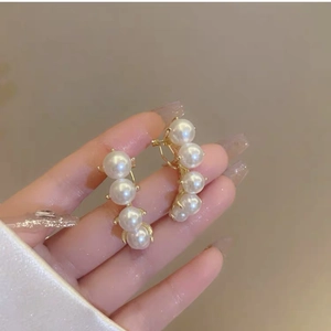 Close-up of elegant gold pearl drop earrings with four white pearls in a vertical curved line