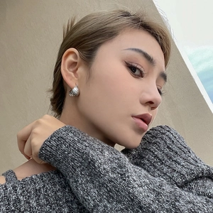 Détail de boucles d'oreilles argentées texturées sur un modèle à l'esthétique minimaliste