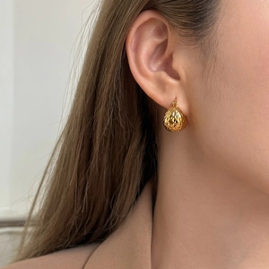 Gros plan de boucles d'oreilles goutte dorées avec motif géométrique texturé