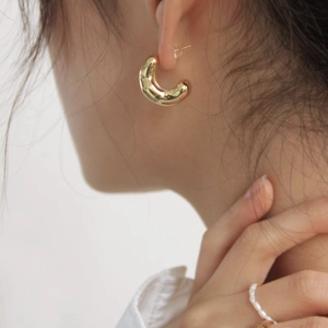 Detail of chunky gold C-shaped hoop earrings paired with a pearl bead ring on model