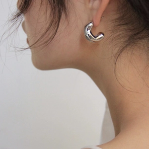 Macro detail of polished irregular silver hoop earrings on a model showing smooth metallic finish