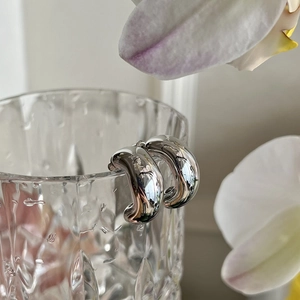 Macro detail of chunky silver hoop earrings with high-polish finish on glass and orchid