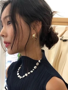 Close-up of model wearing C-shaped gold metal earrings and white baroque pearl necklace