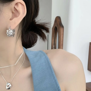 Detail of silver textured cube earrings and liquid silver pendant layered necklace