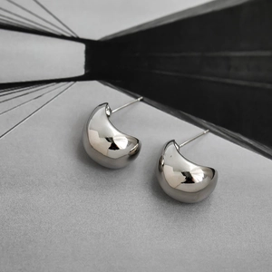 Dettaglio di orecchini a goccia con finitura argento lucido a specchio e design minimalista