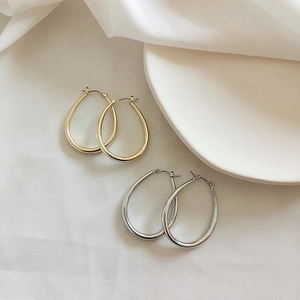Detailed close-up of oval gold and silver hoop earrings on elegant white fabric