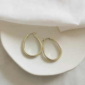 Close-up of gold-plated drop hoop earrings on a ceramic dish with white fabric