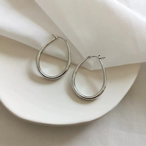 Close-up of polished silver teardrop hoop earrings placed on a white porcelain dish