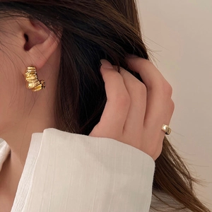 Close-up of golden irregular wavy C-shaped earrings and a matching wide band ring