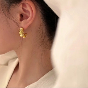 Detailed view of gold C-shaped earrings with unique crinkled texture on an Asian model