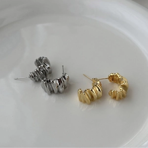 Close-up of irregular textured C-shape stud earrings in gold and silver metal finishes