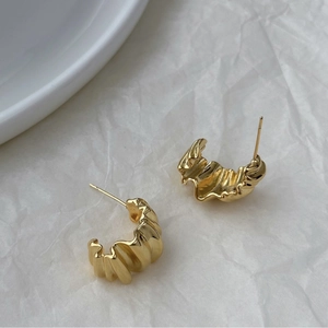 Close-up of golden irregular C-shaped earrings with textured metallic pleats and studs