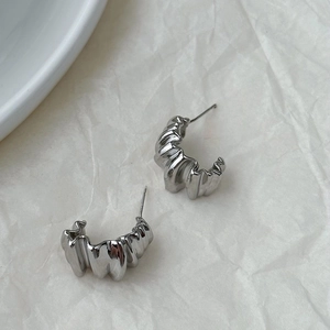 Detail of irregular C-shaped pleated silver metal earrings on white aesthetic background