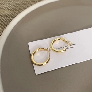 Detail shot of chunky gold hoop earrings on white display card with ceramic plate background