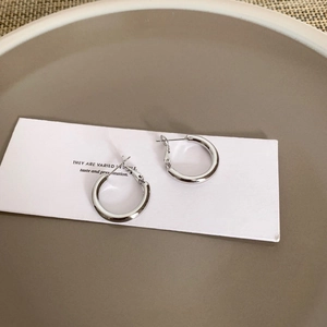 Detailed close-up of thick silver geometric hoop earrings on a minimalist white display card