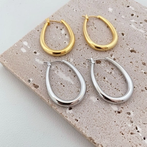 Polished gold and silver oval hoop earrings displayed on textured stone background