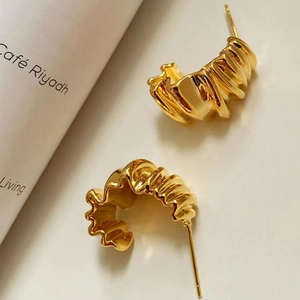 Minimalist gold croissant hoop earrings with textured pleated metal design on a table