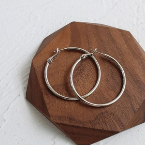 Detailed view of polished large silver hoop earrings on a hexagonal wooden display base