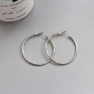 Close-up of polished silver hoop earrings on a minimalist grey surface with a candle