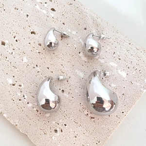 Macro shot of silver teardrop stud earrings in two sizes on a beige travertine stone