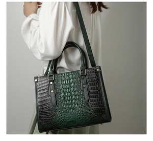 Detail of dark green crocodile embossed tote bag with gold hardware worn by a model