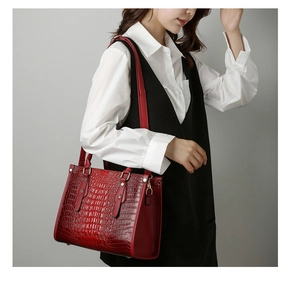 Detail of burgundy crocodile-embossed tote bag featuring gold hardware and handles