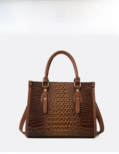 Detail view of deep brown crocodile pattern handbag with sturdy handles and metallic rivets